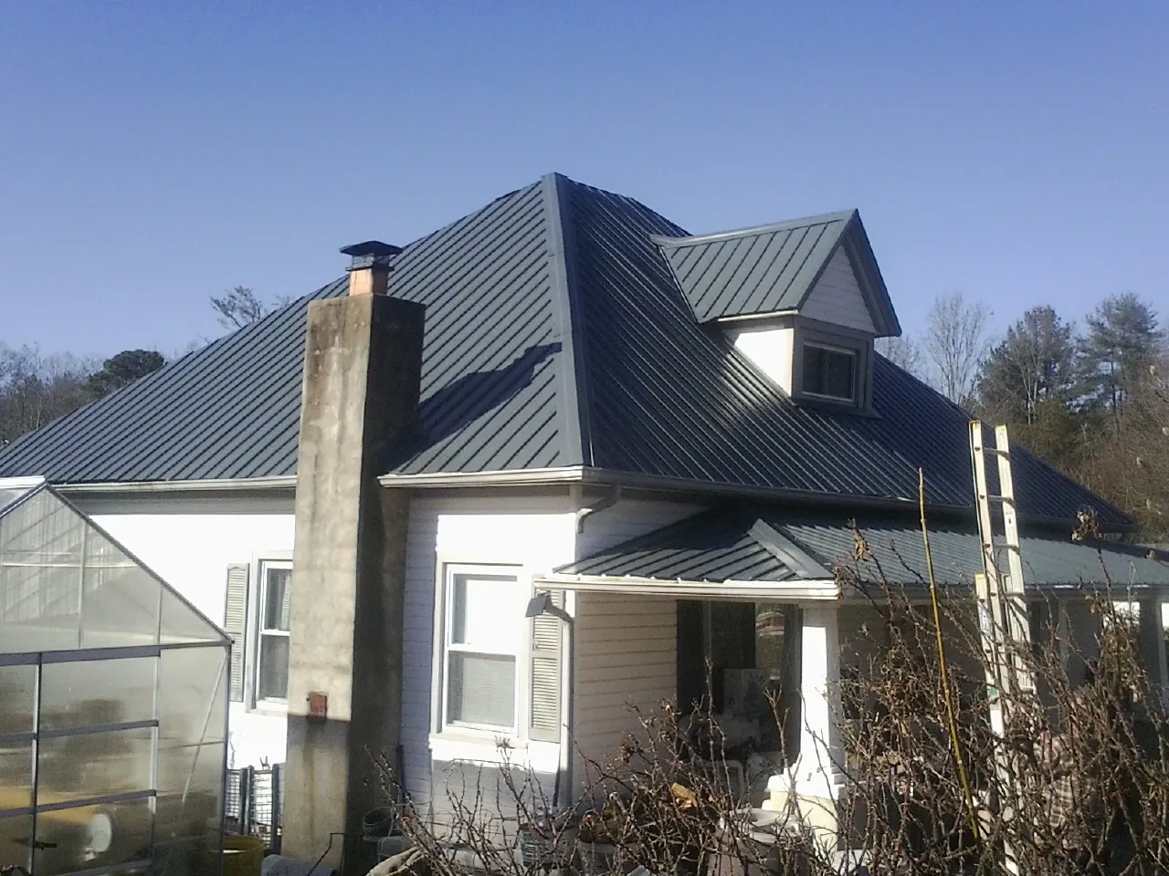 Dark blue standing seam metal roof on a white farmhouse with dormer — Slate & Tile Roof Repair by Roofing Brothers in Aspinwall