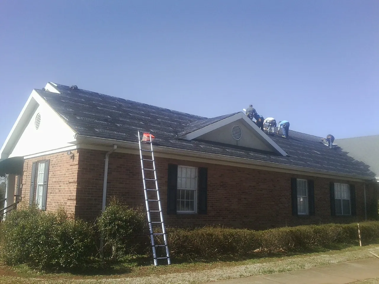 Crew tearing shingles off a brick ranch roof with a ladder set — Emergency Roof Repair work by our crew in Aspinwall