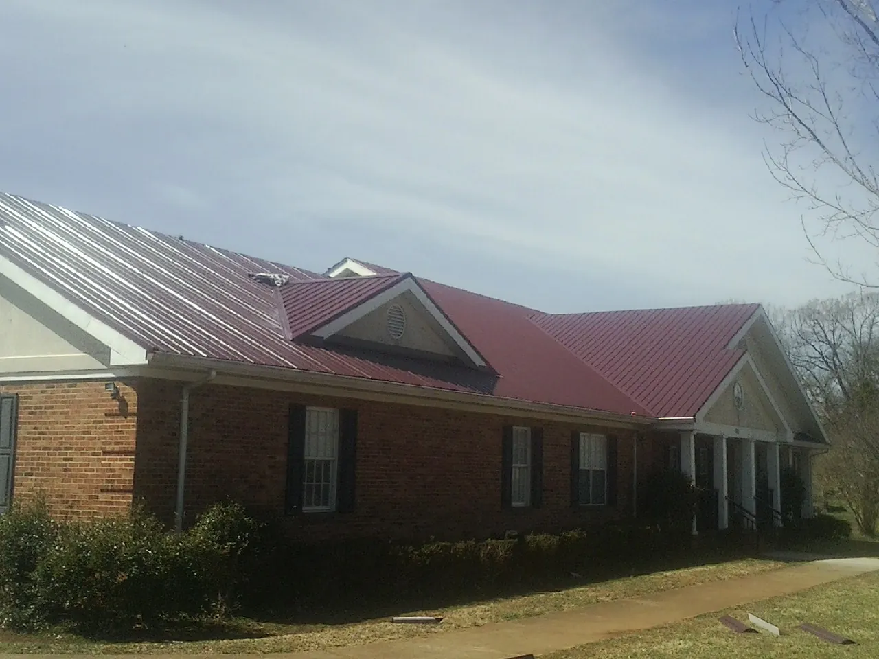 Red metal roof with gabled entries on a long brick building, from a Hail Damage Roof Repair job in Aspinwall