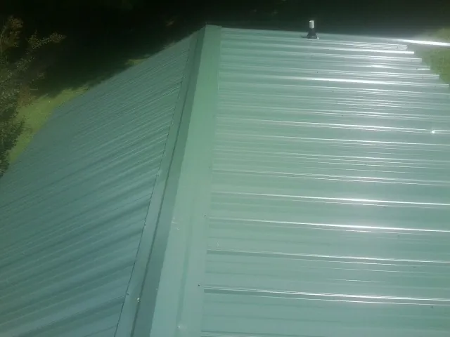 New green metal panels meeting at the ridge of a roof — Flat Roof Repair work by our crew in Aspinwall