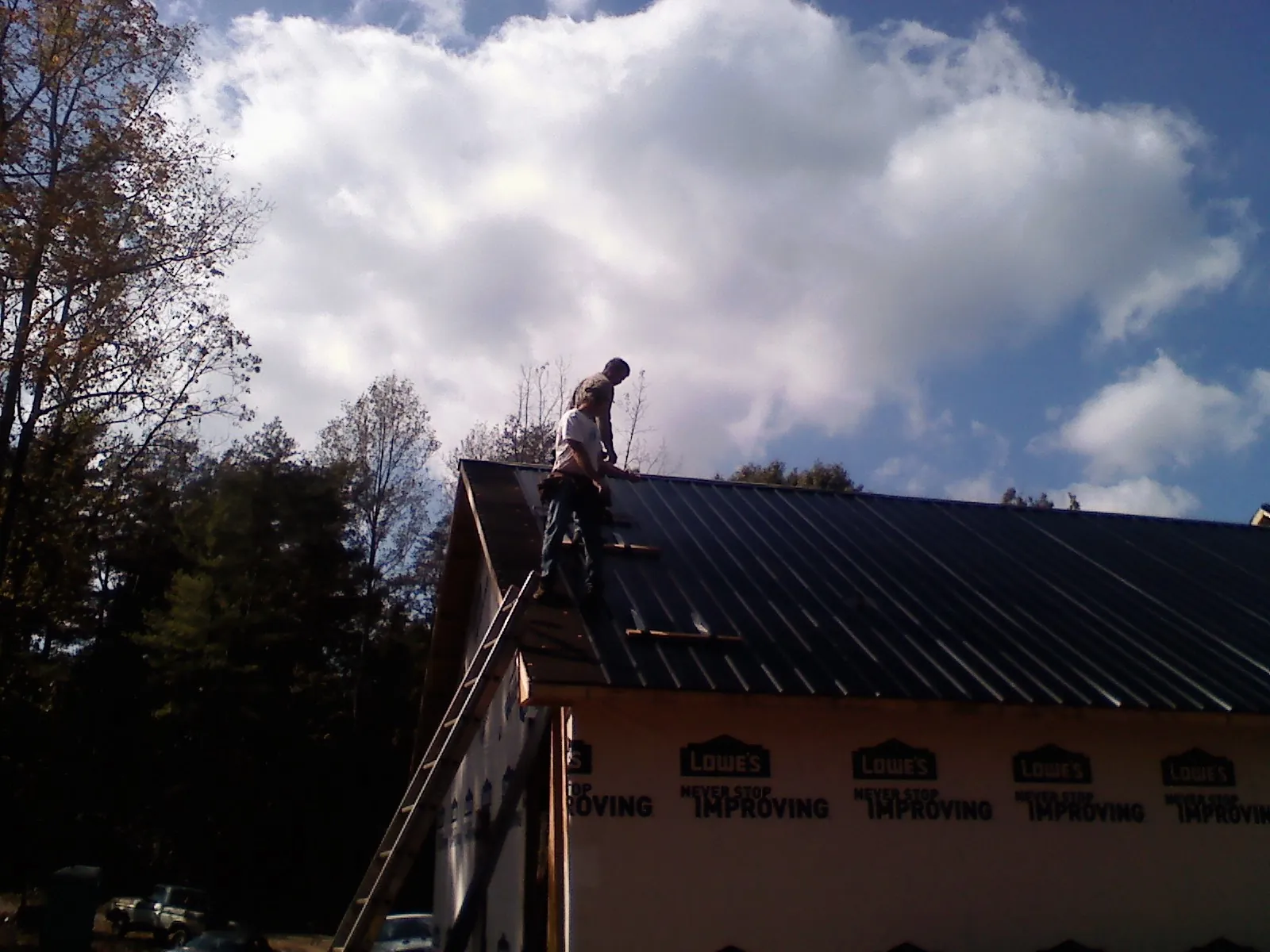 Roofer fastening dark metal panels high against a cloudy sky, from a Roof Inspection job in Aspinwall