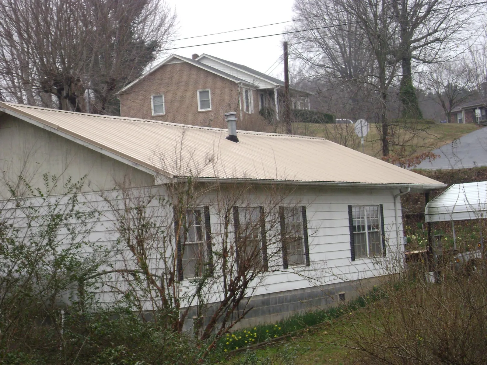 Tan metal roof on a white sided house set into a hillside — Commercial Roofing by Roofing Brothers in Aspinwall
